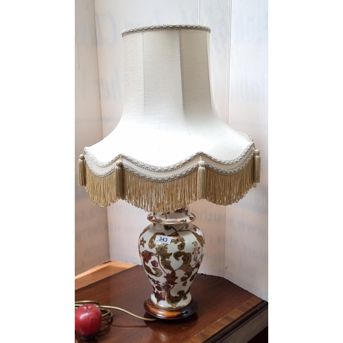 343 - An antique-style Chinese table lamp on a wooden base, with a gilt floral pattern and a cream, fringe... 