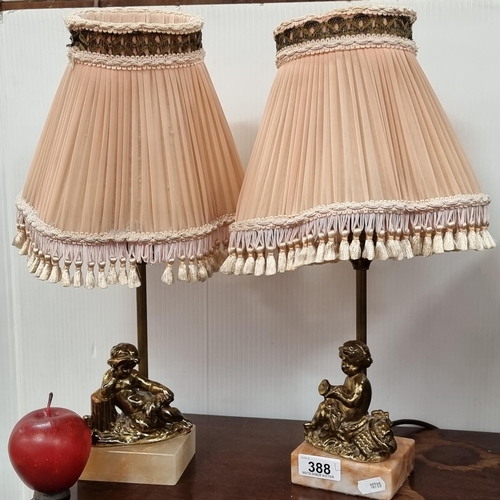 388 - A pair of small brass toned cherub lamps with onyx base, and dusty pink, pleated shades with tassels... 