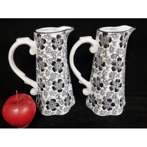 128 - An elegant pair of tall ceramic pitchers with curved scroll handles, and flared bases. Featuring a p... 