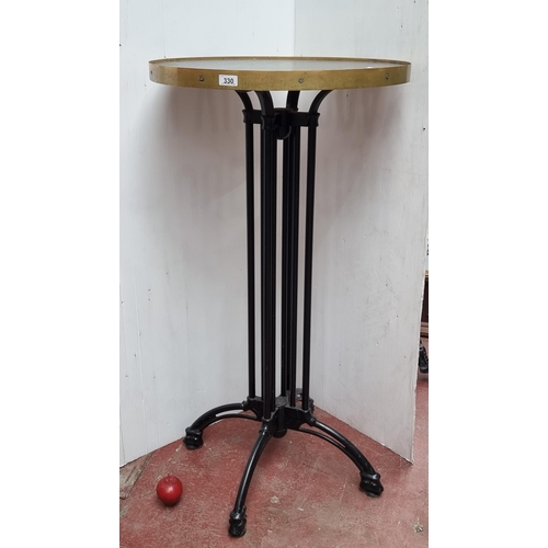 330 - A tall commercial circular bar table with cast metal legs and wooden top with brass edging. This is ... 