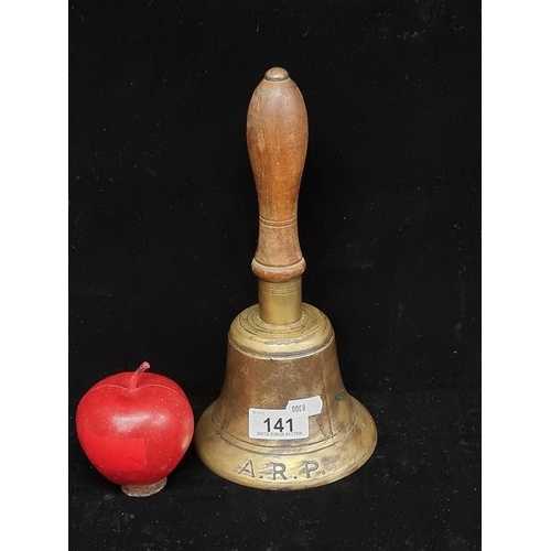 141 - A heavy brass hand bell with turned wooden handle, engraved with the acronym 