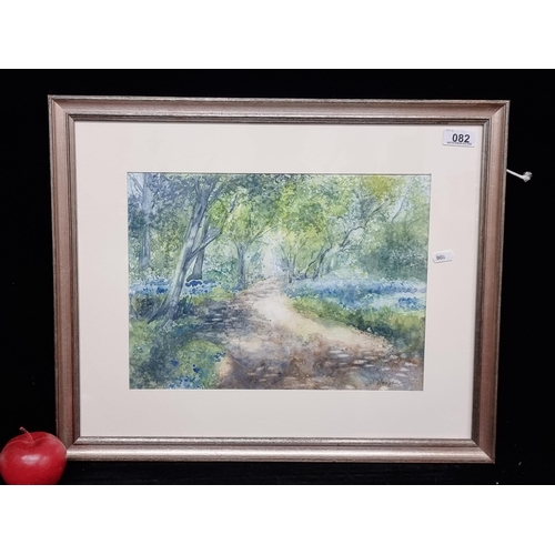 An original watercolour on paper painting titled "Bluebells" by artist M. Morgan and dated to 2017. Features a sunlit trail in a bluebell filled wood in vivid colours.