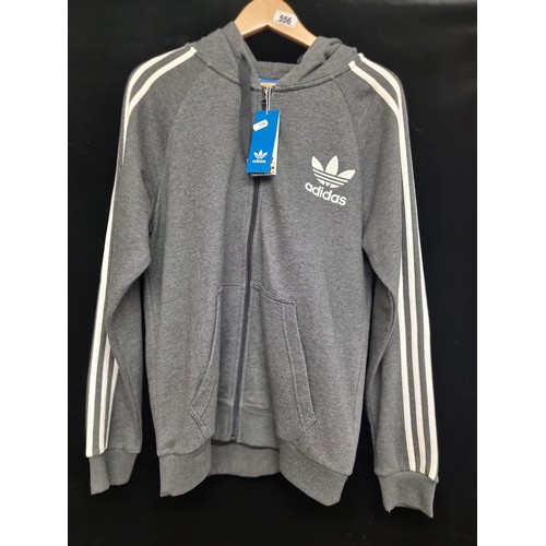 556 - A brand new genuine Adidas zip-up hoodie in UK size Medium. In a grey shade, with iconic stripes and... 