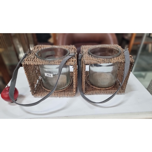 711 - Two garden lanterns with wicker frame and glass inserts to hold pillar candles. Both with grey strap... 