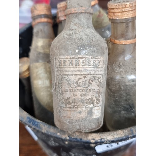 613 - A bucket containing twelve vintage bottles. Brands included are Hennessy, and John Power & Son. Some... 