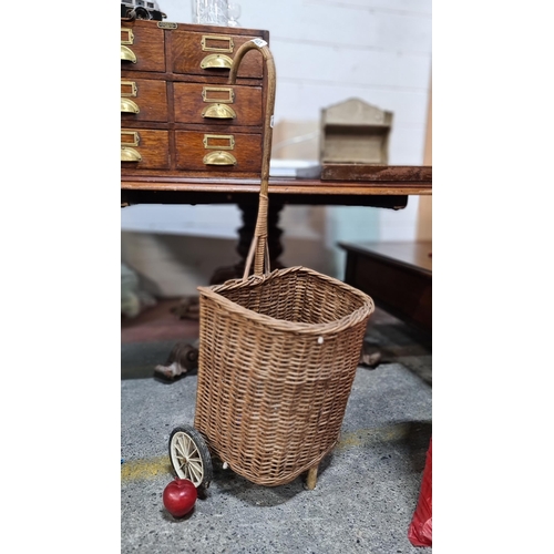 831 - A fantastic wicker trolley on two wheels, with a hooked handle.