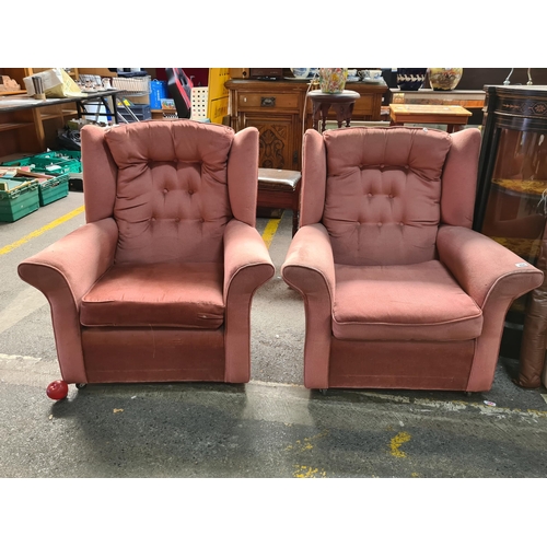 894 - A pair of wing back bedroom chairs, in a dusky rose shade with button back detail. On a set of caste... 