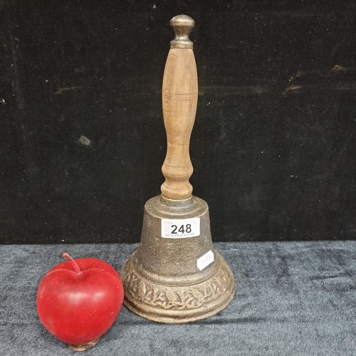 248 - A large metal school bell with a turned wooden handle, with a banded design featuring a bird perched... 