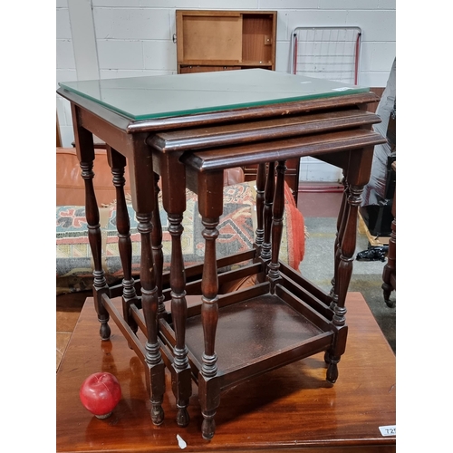 724 - A set of three nesting tables with turned wood legs and a tempered glass top for protection.