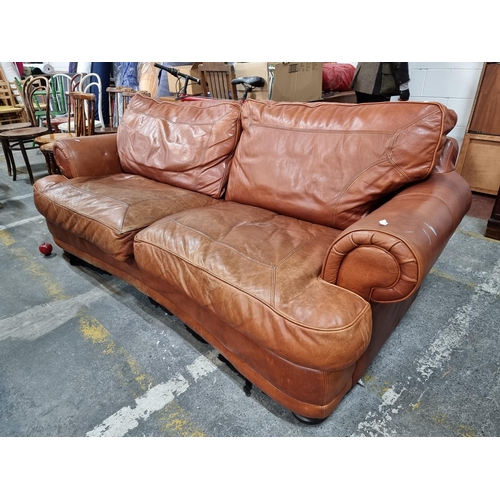 728 - A handsome three seater sofa upholstered in genuine tan leather. A very cosy and comfortable piece.
... 