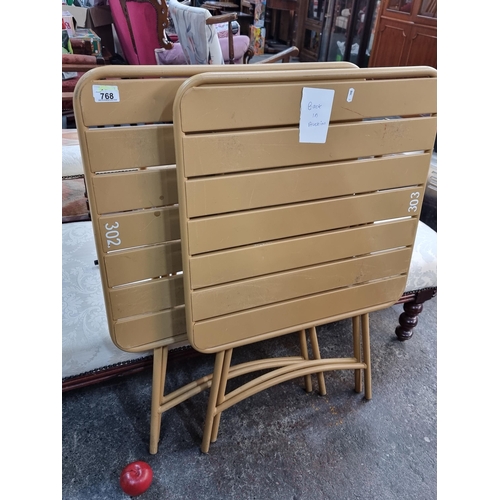 768 - A pair of metal folding tables in a light brown finish. H85cm x L59cm x W59cm