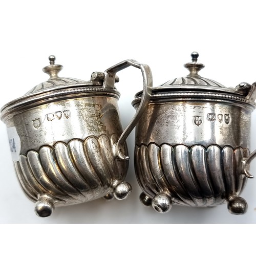 51 - A pair of sterling silver Victorian Mustard pots, each set with scroll ribbed design and handle and ... 