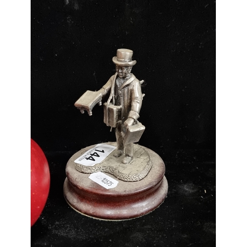 144 - A pewter figurine of a pedlar selling his wares. Mounted on a wooden plinth base.