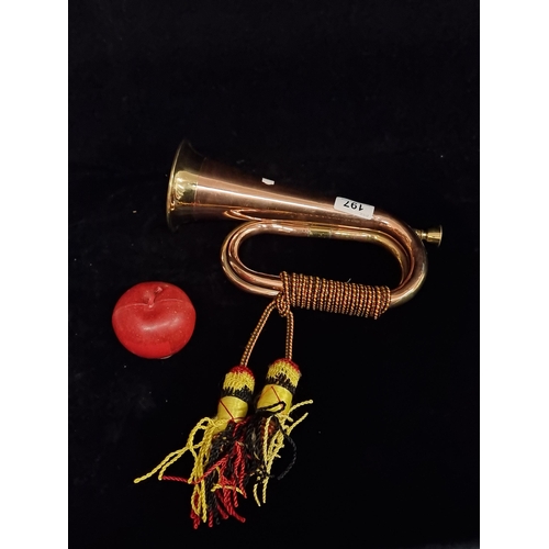 197 - A copper bugle with colourful red, yellow and black tassel.