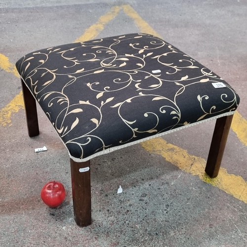 370 - A large footstool with black and gold floral upholstery on a heavy wooden frame.