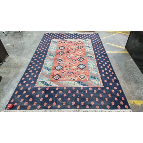 498 - Star Lot : A large Turkish wool blend rug from brand Lyric. In shades of red, turquoise and navy blu... 