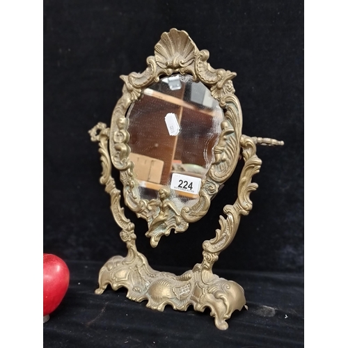 224 - A heavy quality and ornate brass swivel mirror. The frame features foliate, cherub and shell motifs.... 