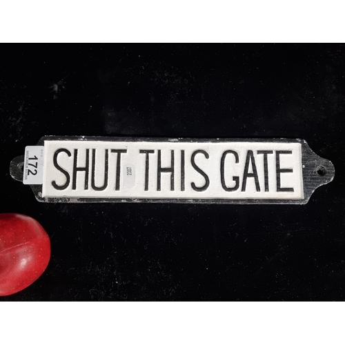 172 - A cast metal wall sign reading 'Shut This Gate'' in black text on a white background.