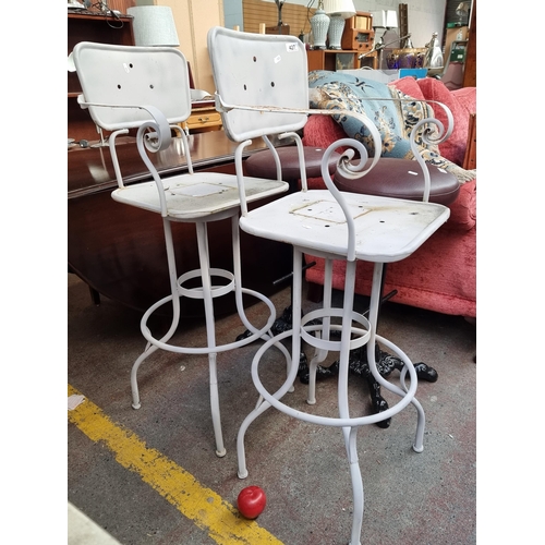 A pair of unusual cast-metal outdoor tall bar-stools. These high stools offer backrest support and a swivel feature. Finished in a taupe brown with footrest to base.
