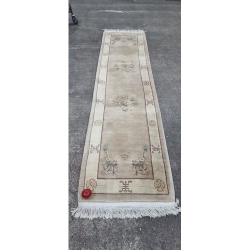 A soft wool hall runner rug featuring a Chinese dragon motif in shades of brown, pastel pink and turquoise against a cream ground. L320cm x W77cm