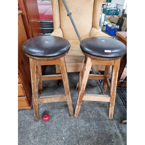 694 - A pair of vintage bar stools. Featuring heavy wooden bases and brass foot rests with a leather uphol... 