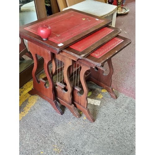 994 - A set of three vintage nesting tables with tooled leather tops in a red finish and lyre supports.