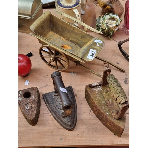 383 - Four vintage items including three vintage hand irons and a brass cart with fully rotational wheels.