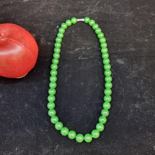 657 - A Chinese  polished green jade n necklace . With polished white metal closure. L47cm Cold to the tou... 