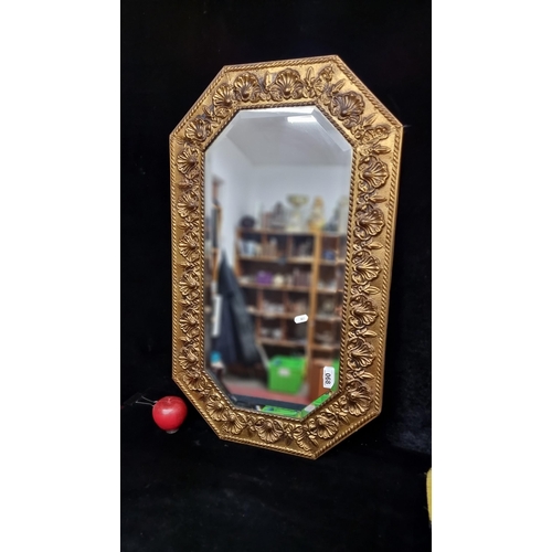 68 - An antique octagonal beveled wall mirror held in an ornate brass toned frame boasting elaborate scal... 