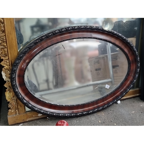 918 - An antique oval wall mirror with beveled glass and lacquered frame boasting carved detailing. 
MM: W... 