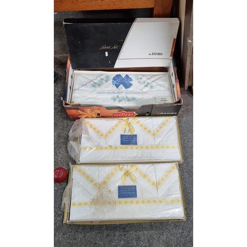 766 - A box containing three vintage sets of embroidered bed linen, all complete in original packaging. On... 