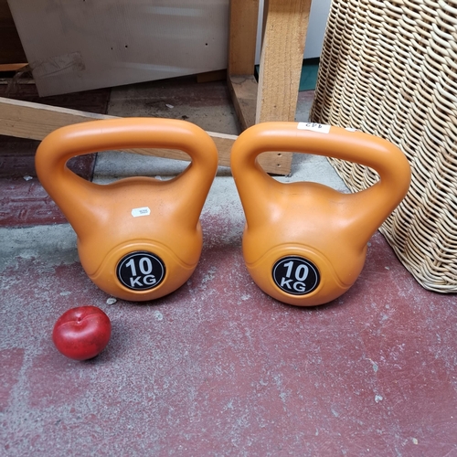 942 - A pair of kettle bells weighing 10kg each, in a bright orange finish.