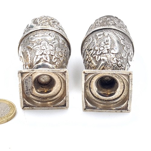 58 - A pair of Victorian sterling silver salt and pepper cruets, featuring a repoussé motif and top finia... 