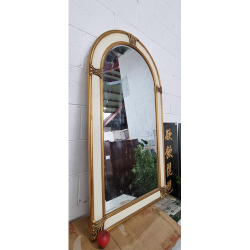 914 - A large striking wall mirror with bevelled glass and a round top. Housed in a wooden frame with crea... 