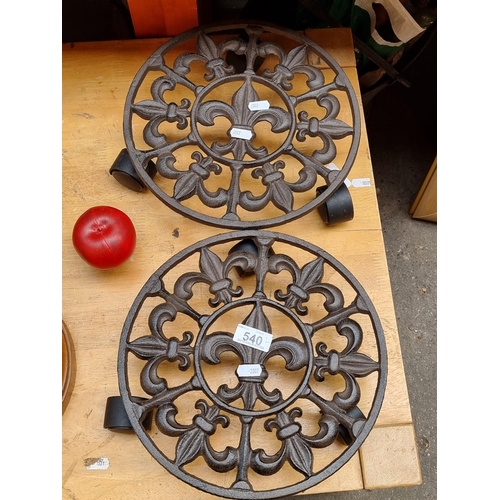 540 - A pair of fleur de lis cast metal transportable plant stands set on three castors each.