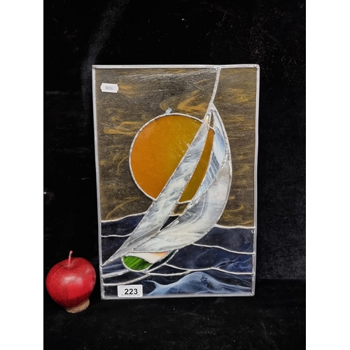 223 - A cheerful stained glass art piece depicting a sailboat against a sunset. H36cm x W25cm