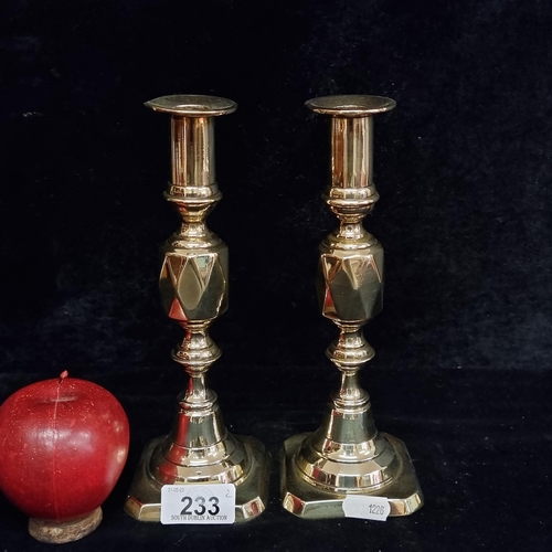 233 - A pair of antique brass Queen of Diamonds candlesticks with a faceted detail to centre.  Nicely poli... 