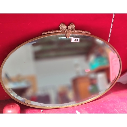 280 - A beautiful antique oval wall mirror with beveled glass and set in a brass frame boasting scalloped ... 