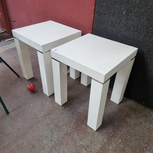 323 - A pair of sleek contemporary side tables with square tops set on thick legs. In a high gloss white f... 