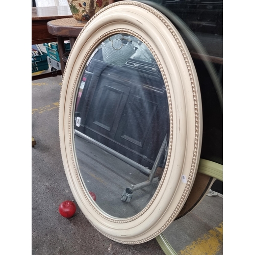 466 - A charming oval wall mirror set in a cream frame with carved beaded detail and beveled glass. W88cm ... 