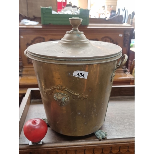 494 - A vintage brass coal scuttle featuring a finial to lid, handles and ram masks to sides and lion paw ... 