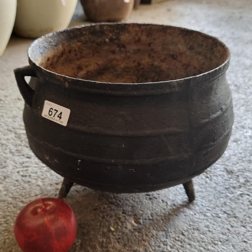 674 - A heavy cast metal cauldron stood on three feet and featuring two handles to sides. Ideal for use as... 