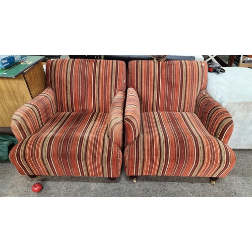 826 - Two large armchairs upholstered in a striped red and beige fabric. Held on bun feet on brass castors... 