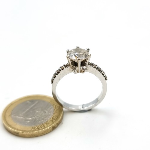 9 - A striking 9 carat White Gold Solitaire ring, set with a central White Sapphire and gem set shoulder... 