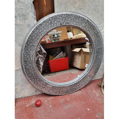 265 - A large striking circular wall mirror housed in an ornate silver toned frame with embossed floral mo... 