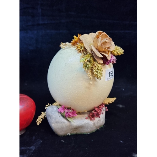 158 - A vintage, hollow Ostrich egg mounted on a stone base and adorned with dried flowers. H18cm