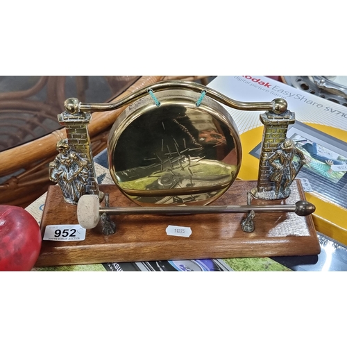 952 - A tabletop brass dinner gong with beater. Featuring figural supports and wooden base.