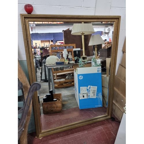 852 - A very large wall mirror with bevelled glass housed in a wooden gilded frame. MM: 133cm x 101cm In g... 