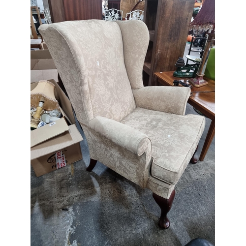 865 - A vintage wingback armchair with a soft beige upholstery and cabriole legs. In good condition.