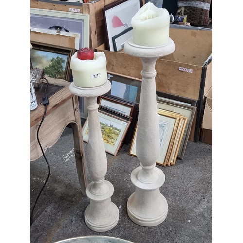 977 - A pair of graduating pillar candle holders in a stone effect and bevelled detail. Both supplied with... 